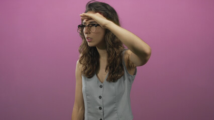 Naklejka premium Woman wearing glasses shielding eyes with hand over forehead in studio; curiosity exploration discovery.