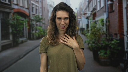 Fototapeta premium Woman places hand on chest while standing in a narrow street amid brick building facades at daylight; gratitude.