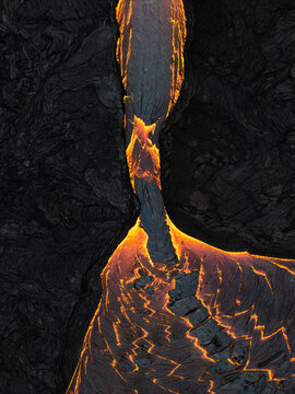 Aerial view of glowing lava snaking through the dark, jagged landscape, stark contrast between fiery orange and charcoal black, Grindavik, Iceland.