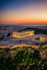 Aerial view of the illuminated Parthenon Temple at the Acropolis of Athens, Greece, during dusk with the city skyline behind