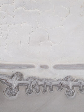 Aerial view of the cracked, bleached earth meeting the dark, water-filled trenches in a stark contrast of textures and tones, Old Chandler, Western Australia, Australia.