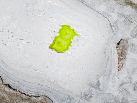 Aerial view of a bright green pool contrasting against the stark white and grey cracked earth of the Old Chandler Potash Mine Site, Old Chandler, Western Australia, Australia.