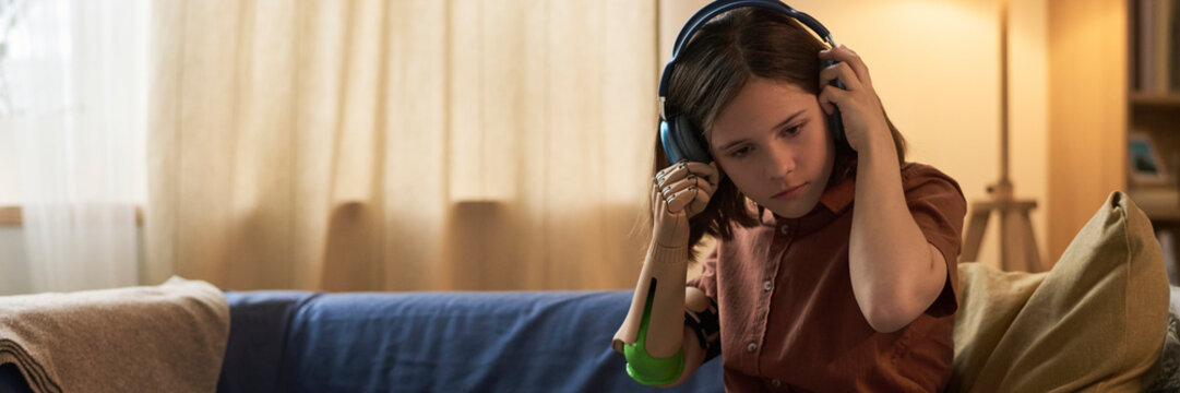 Girl with prosthesis listening to music on headphones relaxing indoors