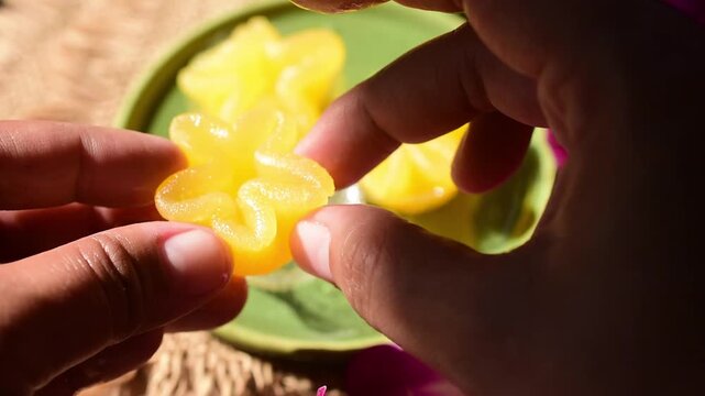 Hand holding Thong Yip, a traditional Thai flower-shaped egg yolk dessert. This golden auspicious sweet represents wealth and prosperity in Thai culture. Soft focus background with vibrant colors.