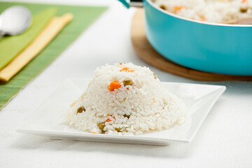 Portion of traditional Turkish rice pilaf with vegetables served on a white square plate, bright...