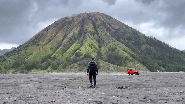 Traveler walking across Sea of Sand toward Mount Batok near Mount Bromo in East Java, Indonesia. Dramatic volcanic landscape in Southeast Asia. Concepts of travel, nature, and adventure.
