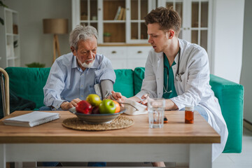 Fototapeta premium Home healthcare professional checking senior man's blood pressure