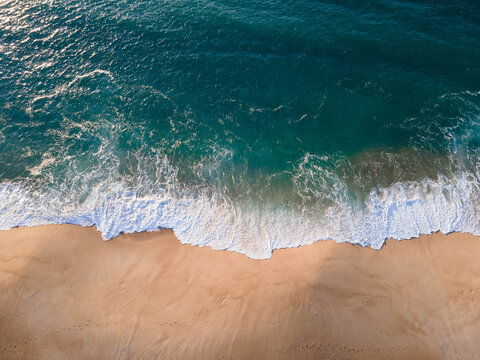 Aerial view of turquoise waters crashing onto the golden sands, creating a mesmerizing spectacle of nature's raw power, Nazare, Leiria District, Portugal.