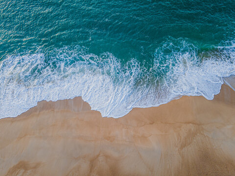 Aerial view of the beach where the turquoise ocean meets the golden sand, creating a striking contrast, Nazare, Leiria District, Portugal.