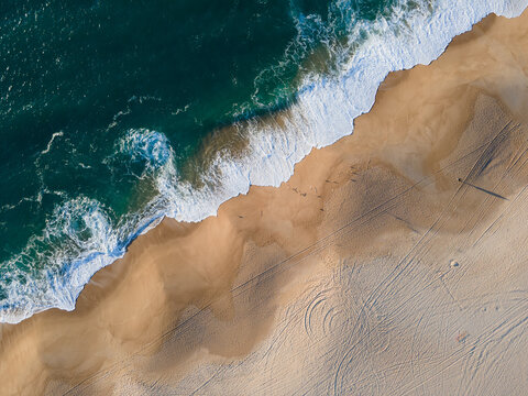 Aerial view of turquoise waves crash against the golden shore, creating a stunning contrast, Nazare, Leiria District, Portugal.