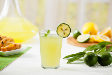 Fototapeta premium Fresh homemade lemonade or lime juice in a glass with lemon and lime slices on a wooden board, bright garden background.