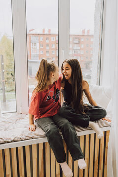 Sisters having fun and hugging on windowsill at home