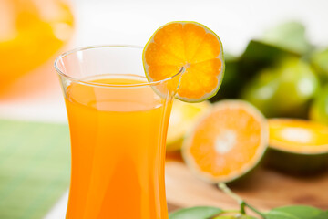 Fototapeta premium Freshly squeezed citrus juice in a glass and glass carafe with orange and lime fruits on a wooden table, garden background.