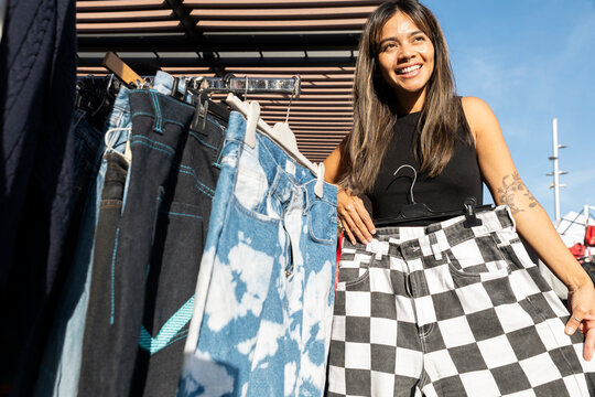 Smiling person shopping for checkered pants at flea market outdoors