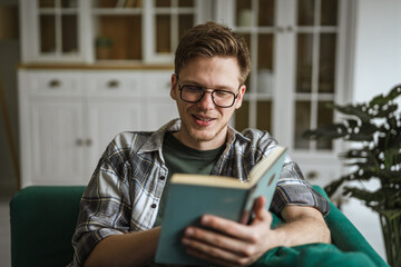 Young man wearing glasses reading a book at home