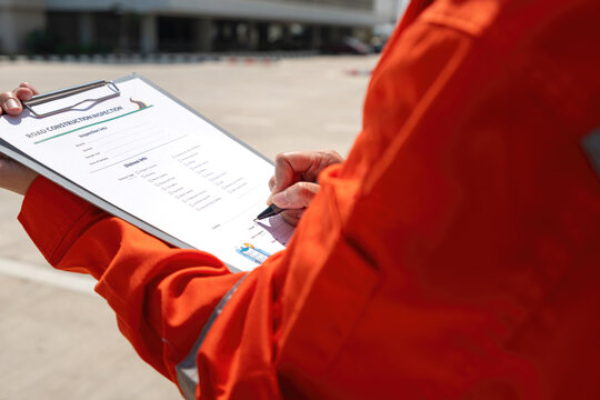 An civil engineer is checkling on road inspection checklist to verify the quality of building job with blurred background of new concrete road. Industrial working scene, close-up and selective focus.