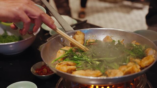 Chefs prepare traditional cha ca fish with turmeric and fresh herbs at Cha Ca Thang Long restaurant in Hanoi, Vietnam, showcasing a classic northern Vietnamese culinary experience.