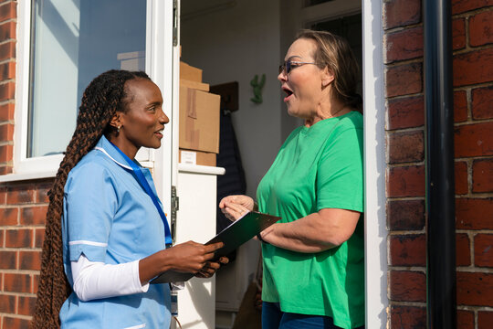 Health worker talks to a woman at her door during a home visit in a city neighborhood