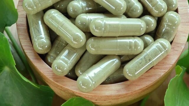 Herbal capsules contain powdered gotu kola and gotu kola leaves in a wooden bowl.
