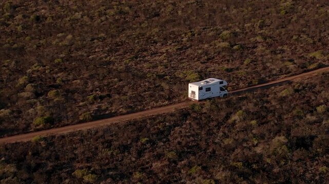 Camper driving along sandy plateau above Fal&eacute;sias da Arriba F&oacute;ssil in Costa da Caparica, Almada, Portugal, crossing Atlantic fossil cliff landscape with Mediterranean scrub vegetation, drone tracking