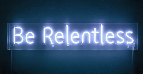 Obraz premium Bright neon sign displays text Be Relentless against dark blue wall. Simple, motivational message radiates energy.