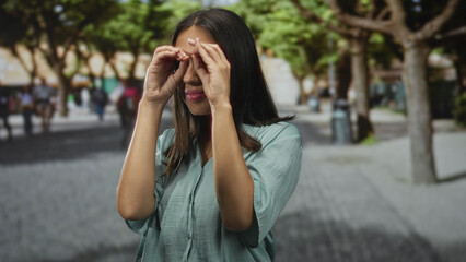 Fototapeta premium Woman forms hand binoculars with hands on a city street, forearms visible near trees and benches; playful curiosity.