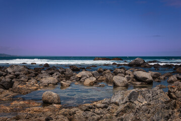 A glimpse of the Pacific Ocean in central Chile at dawn with rocks and pink clouds.