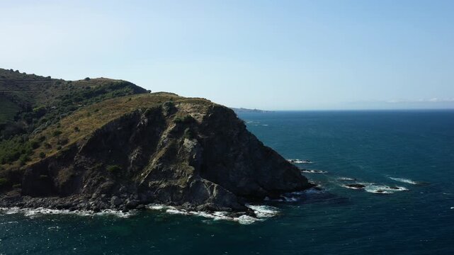 Wide view of the rugged coastline and deep blue Mediterranean Sea near Banyuls sur Mer, France, under a clear sky. The dramatic cliffs and waves create a striking natural landscape.