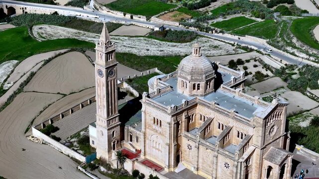 Majestic Ta Pinu National Shrine on Gozo Island Malta captured from a high aerial perspective under the bright Mediterranean sun during a peaceful spring day featuring golden limestone and green field