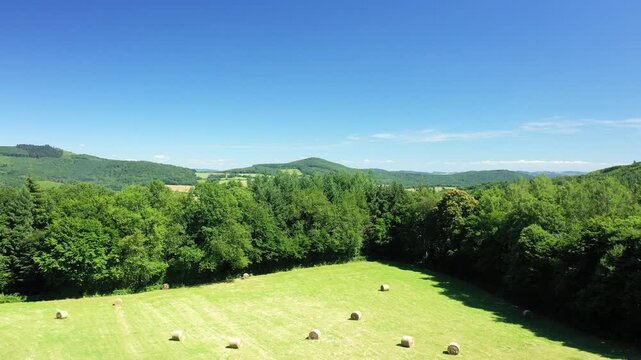Lush green hills, forests, and hay bales under a clear blue sky in the Morvan countryside, France. Peaceful rural scenery with vibrant summer colors.