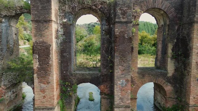 Cinematic drone tracking shot to the right along the ancient Roman Aqueduct of Nicopolis, featuring the repeating red brick arches over the Louros river in Epirus Greece.