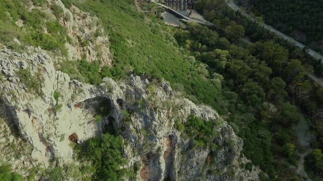 Cinematic drone approach starting from the iconic rock cross formation, revealing the Roman Aqueduct of Nicopolis and the village of Agios Georgios in Epirus Greece amidst a lush river valley.