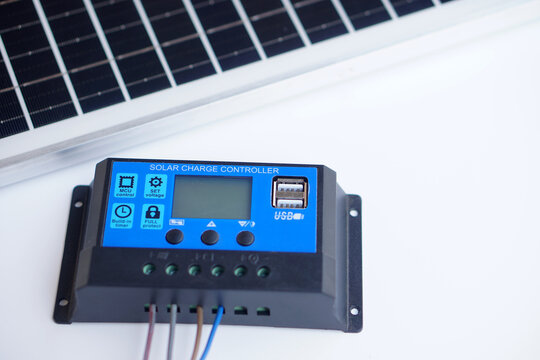 Solar charge controller with USB port connected to wiring, placed near solar panel. Renewable energy equipment for battery charging system, isolated on white background.