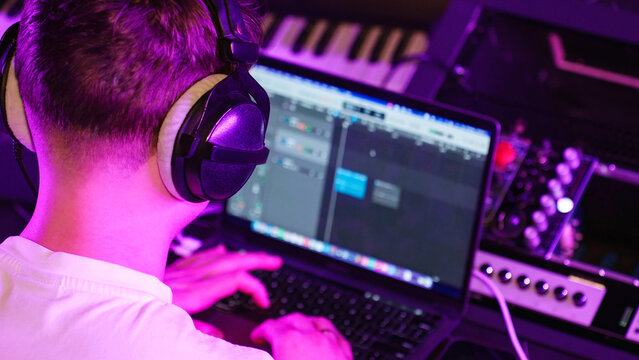 Young Producer Focuses Editing Track, Headphones On. Neon Studio Light, Digital Music Creation, Modern Workflow. Recording studio.