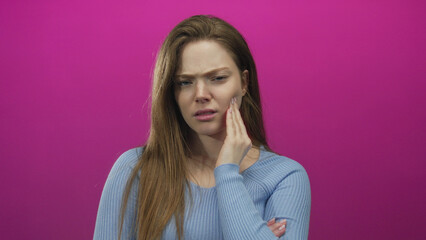 Obraz premium Young caucasian woman with pained expression hand on cheek in pink studio set; discomfort toothache.