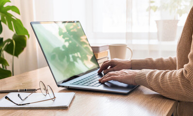 Womens hands typing on laptop keyboard, working remotely from home office desk with mug and...