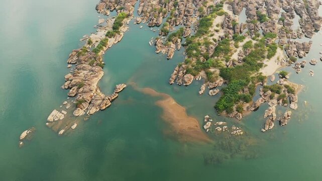 Drone shot of rocky islets and green vegetation in the Mekong River near Champassak, Laos. Clear water surrounds the natural formations, creating a tranquil landscape.