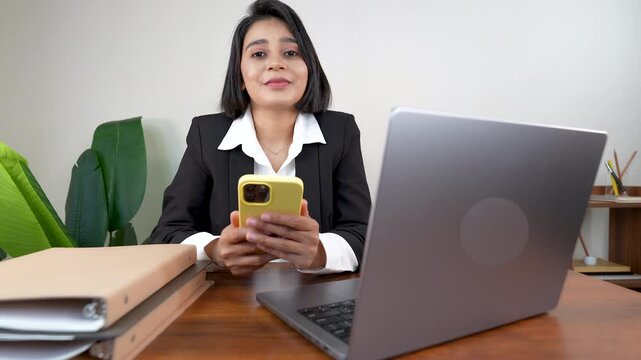 Close up of happy smiling young successful working business woman manager leader boss sits on chair at workplace desk hold cellphone looking at camera with positive face expression.