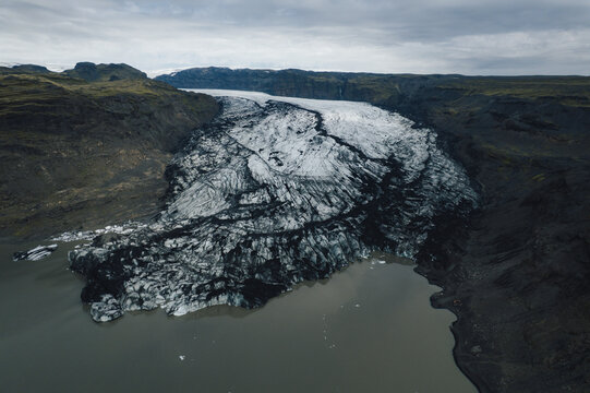 Aerial view of glacial ice grinding through the landscape, a stark contrast between the dark volcanic earth and the pale blue ice, Myrdalshreppur, Iceland.
