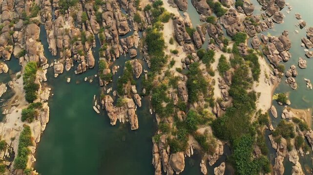 Drone shot of the Mekong riverbed with exposed rocks and patches of vegetation in Champassak, Laos. Unique natural landscape with water channels and rugged stone formations.