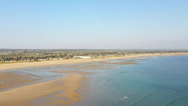 Aerial view of Grande Plage de Barneville with wide sandy beach, gentle waves, and coastal village under a clear blue sky.