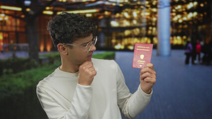 Naklejka premium Man holds austrian passport and visa while resting hand on chin gesture in street; hesitant travel uncertainty.