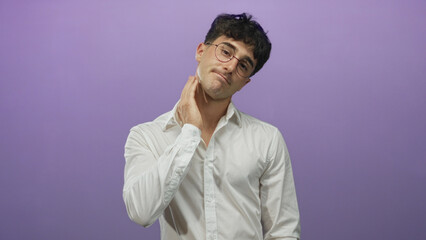 Fototapeta premium Young hispanic man in white shirt and round glasses with hand on neck and fingers touching throat in a purple studio; discomfort.