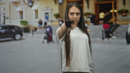 Obraz premium Young woman pointing finger at camera on building steps wearing white tshirt; defiance confrontation.