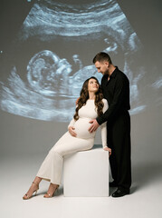Pregnant woman in white dress and partner enjoying ultrasound photo  