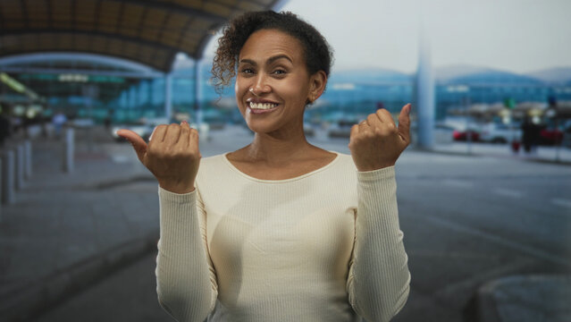 Woman smiling with open palms and hands raised in inviting gesture at airport terminal pickup area; travel welcome.