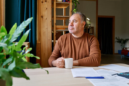 Man sitting at table at home reflecting on bills and household finances