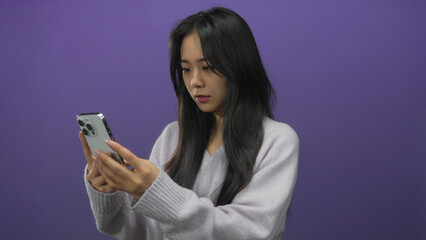 Young woman with cellphone against purple background appearing confused isolated indoors