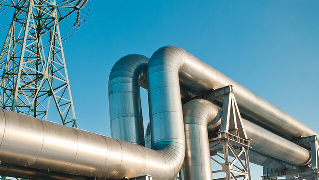A close-up of a pipeline and a power transmission tower against a blue sky