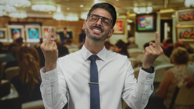 Man wearing glasses and earring with white shirt and tie shows both middle fingers in building; defiance.